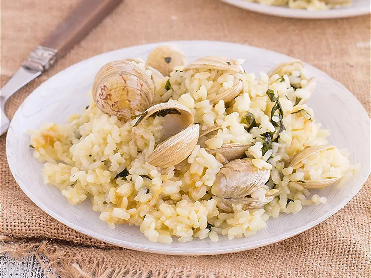 Delicioso arroz con almejas, un plato cremoso y lleno de sabor marino, adornado con conchas abiertas y perejil fresco.