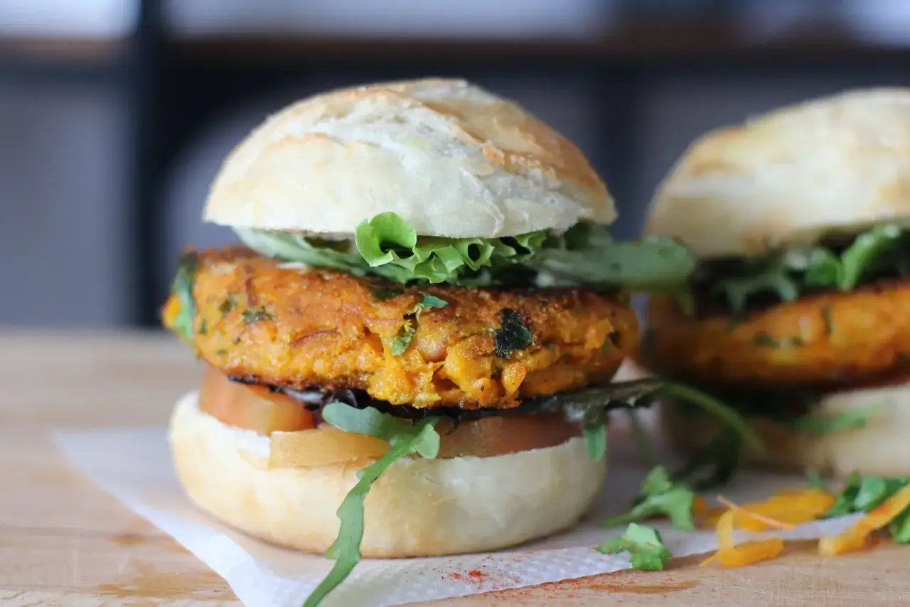 Deliciosa hamburguesa vegana con pan artesanal, lechuga fresca, rodajas de tomate y una jugosa torta de zanahoria y especias.
