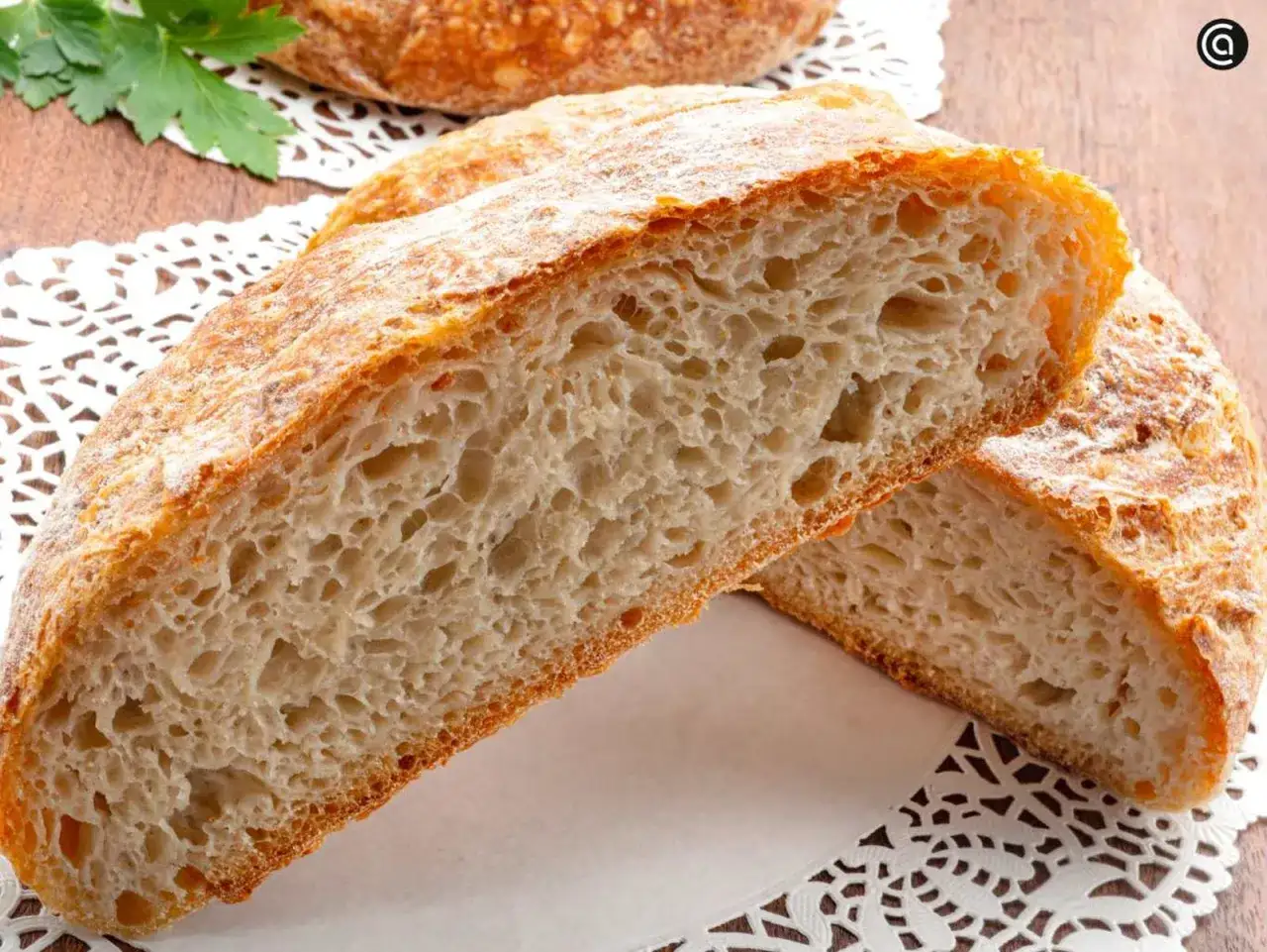 Un pan de papa rústico, cortado por la mitad, revela una miga aireada y una corteza dorada. Perfecto para untar.
