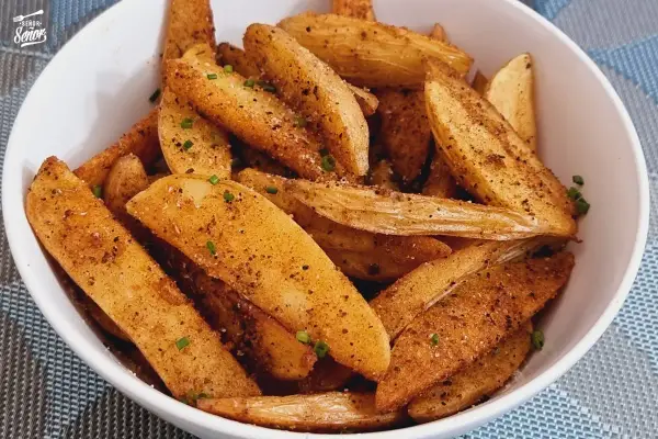 Un tazón lleno de patatas deluxe crujientes, sazonadas con especias y hierbas frescas.